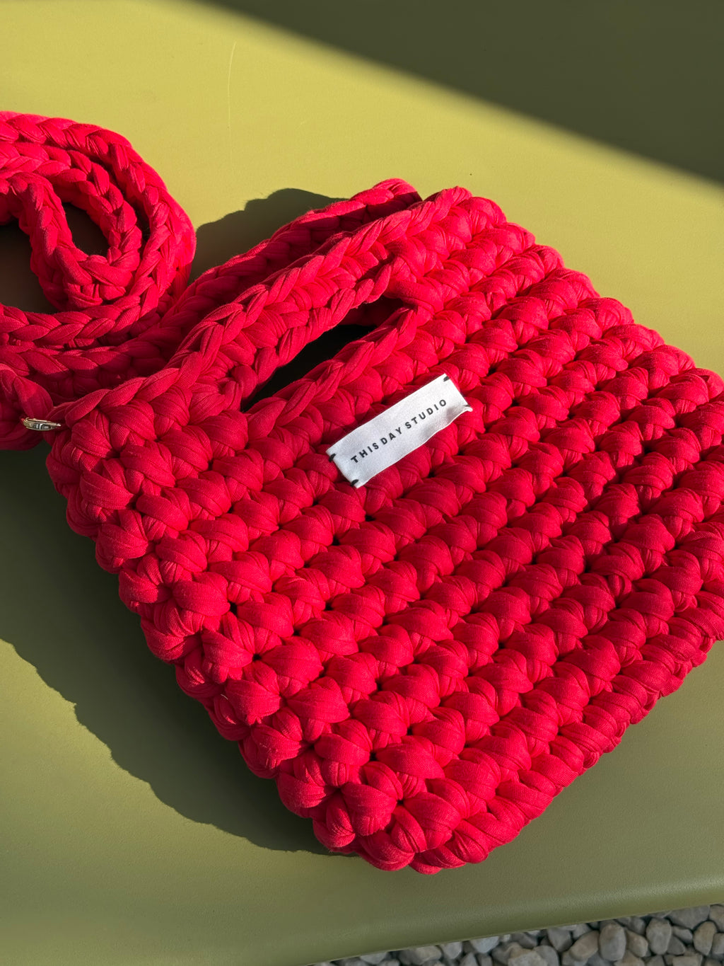 A bright pink chunky-knit shoulder bag with a white brand label reading 'FURRAY STUDIO', resting on a yellow-green surface under direct sunlight.