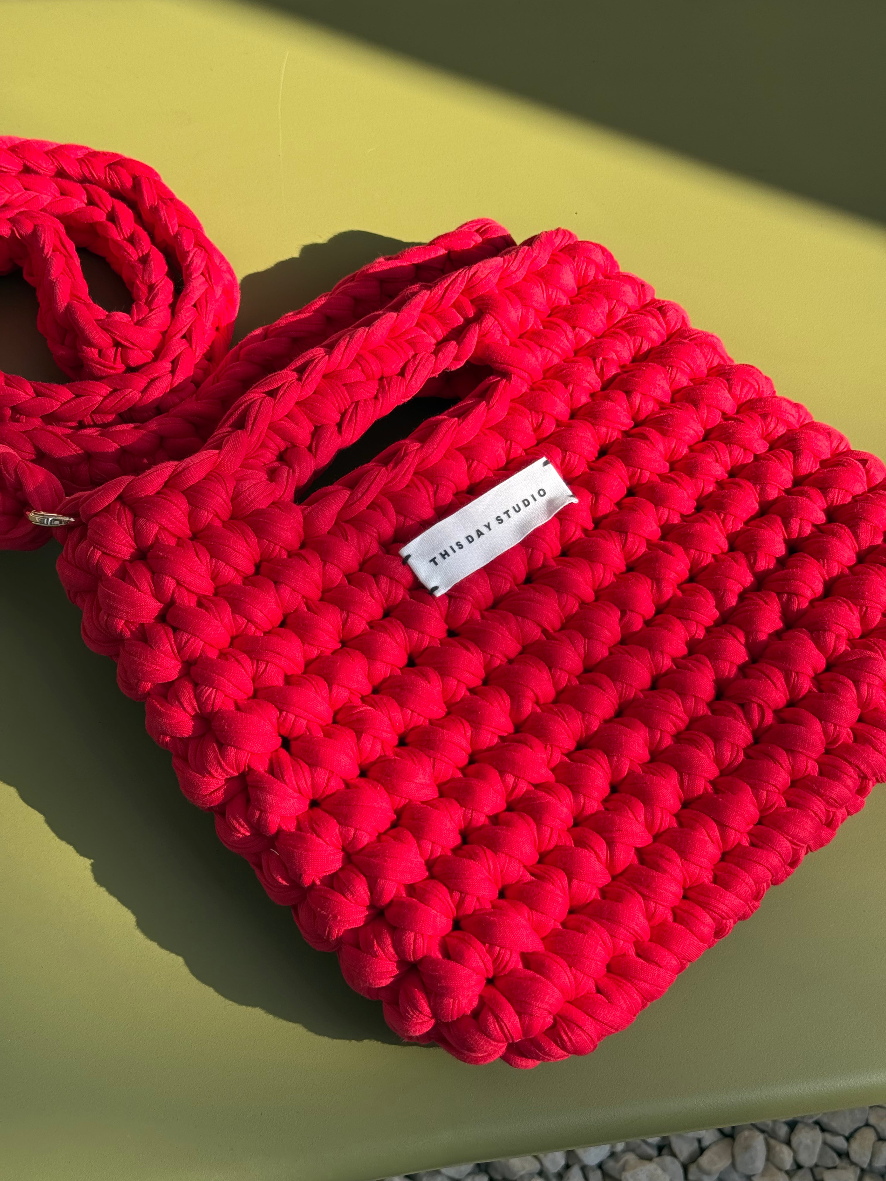 A bright pink chunky-knit shoulder bag with a white brand label reading 'FURRAY STUDIO', resting on a yellow-green surface under direct sunlight.